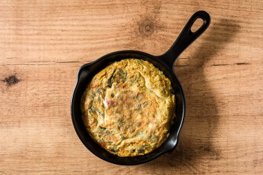 Yumurta ve ahşap masa üzerinde bir Demir Tavada sebze frittata yapmış. Üstten görünüm. 