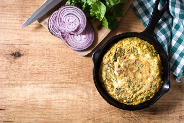 Yumurta ve ahşap masa üzerinde bir Demir Tavada sebze frittata yapmış. Üstten görünüm. Boşaltmak