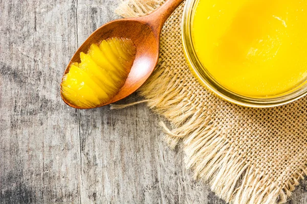 Ghee veya kavanoz ve tahta kaşık ahşap masa üzerinde eritilmiş tereyağı. Üstten görünüm. Boşaltmak