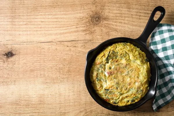 Yumurta ve ahşap masa üzerinde bir Demir Tavada sebze frittata yapmış. Üstten görünüm. Boşaltmak