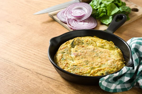 Yumurta ve ahşap masa üzerinde bir Demir Tavada sebze frittata yapılmış. 