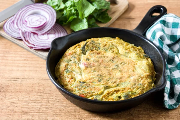 Yumurta ve ahşap masa üzerinde bir Demir Tavada sebze frittata yapılmış. 