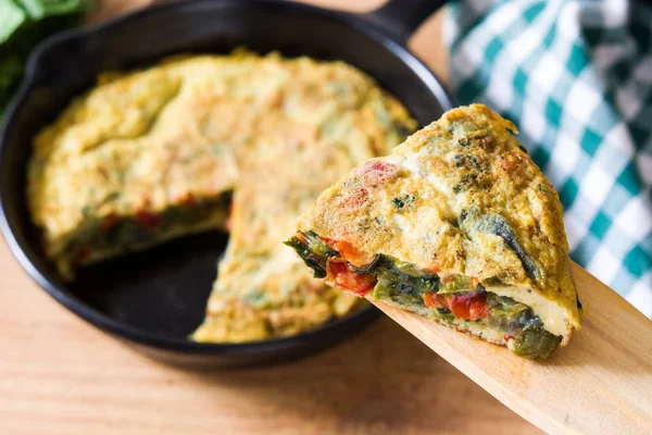 Yumurta ve ahşap masa üzerinde bir Demir Tavada sebze frittata yapılmış. 