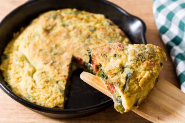 Yumurta ve ahşap masa üzerinde bir Demir Tavada sebze frittata yapılmış.