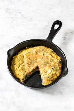 Yumurta ve beyaz mermer üzerinde bir Demir Tavada sebze frittata yapılmış