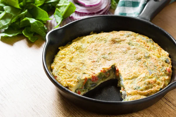 Yumurta ve ahşap masa üzerinde bir Demir Tavada sebze frittata yapılmış.