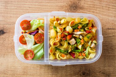 Beslenme çantası ile sağlıklı yiyecekler yemeye hazır. Ahşap masa üzerinde makarna salatası. Üstten görünüm