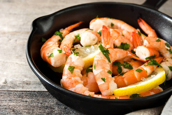 Жареные креветки, петрушка и лимон в железной сковороде на деревянном столе
. 