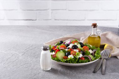 Siyah zeytin, domates, beyaz peynir, salatalık ve gri arka plan üzerine soğan taze Yunan salatası plaka. Boşaltmak