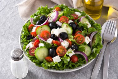 Taze salata tabak içinde siyah zeytin, domates, beyaz peynir, salatalık ve gri arka plan üzerine soğan ile. 