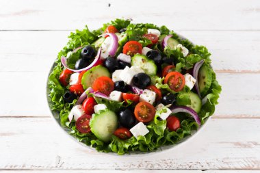 Taze salata tabak içinde siyah zeytin, domates, beyaz peynir, salatalık, Beyaz ahşap zemin üzerine soğan ile 