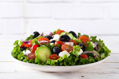 Taze salata tabak içinde siyah zeytin, domates, beyaz peynir, salatalık, Beyaz ahşap zemin üzerine soğan ile 