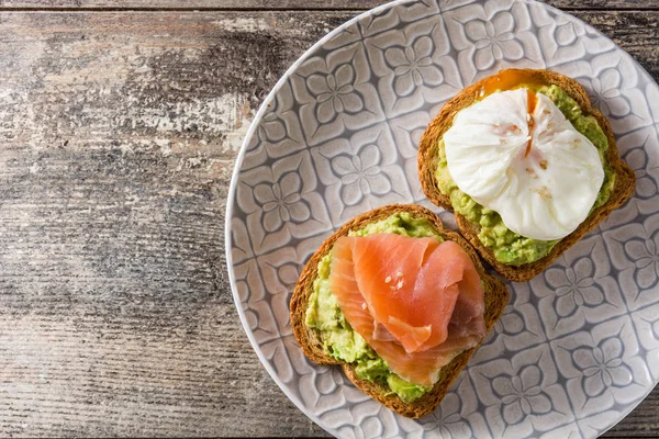 Toasted breads with poached eggs, avocado and salmon in plate on wooden table. Top view. Copyspace