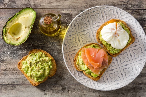 Toasted breads with poached eggs, avocado and salmon in plate on wooden table. Top view