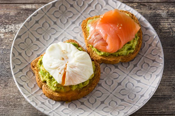 Toasted breads with poached eggs, avocado and salmon in plate on wooden table. Close up