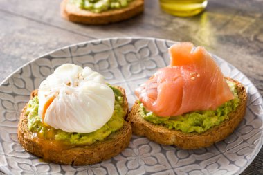 Tahta masa üzerinde tabakta haşlanmış yumurta, avokado ve somon ile tost ekmek.