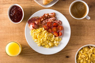 Sahanda yumurta, pastırma, domates, kahve, portakal suyu, kruvasan ve tahta masada Mısır gevreği ile kahvaltı. Üstten görünüm