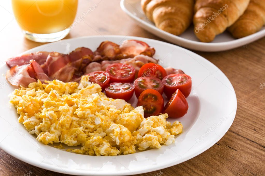 Breakfast with scrambled eggs, bacon, tomatoes,orange juice and croissant on wooden table. 
