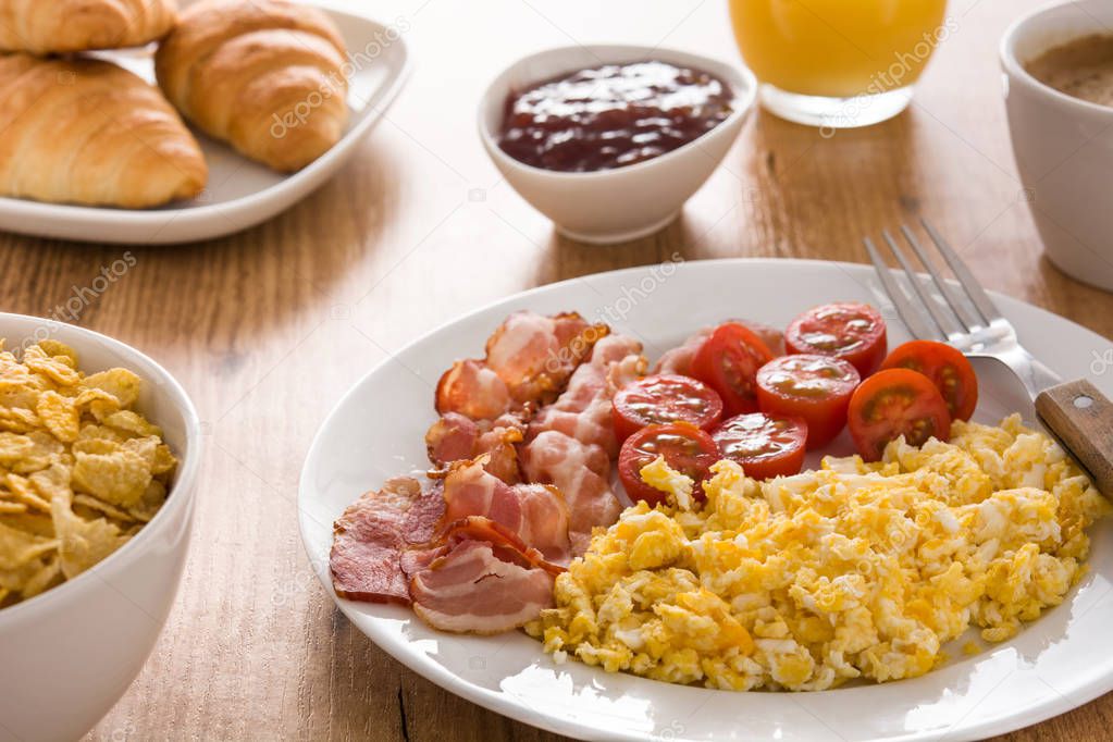 Breakfast with scrambled eggs, bacon, tomatoes,orange juice and croissant on wooden table. Close up