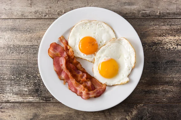 Fried eggs and bacon for breakfast on wooden table. Top view