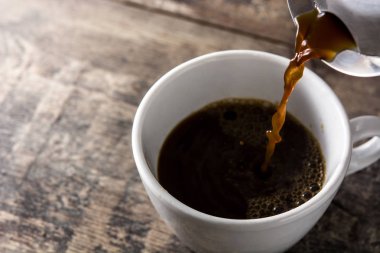 Ahşap masa üzerinde bir fincan sıcak kahve dökme.