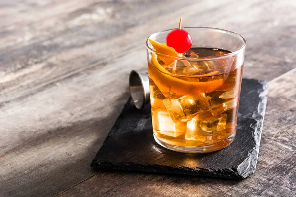 Old fashioned cocktail with orange and cherry on wooden table. Copyspace