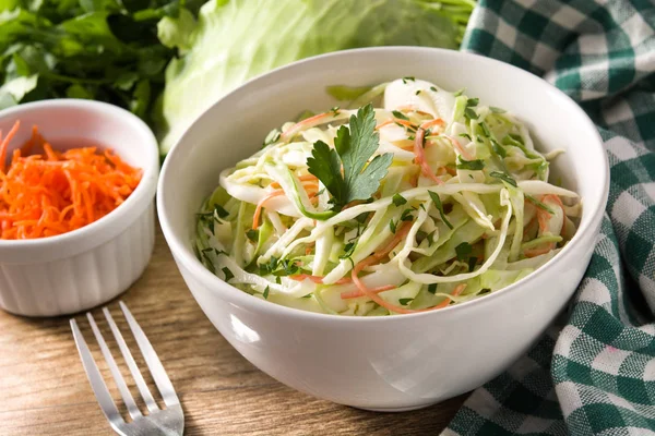 Coleslaw salad in white bowl on wooden table. Close up