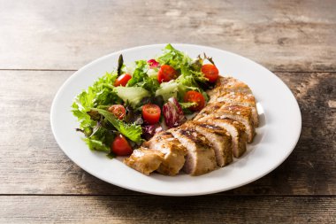 Ahşap masa üzerinde bir tabak üzerinde sebze ile ızgara tavuk göğsü