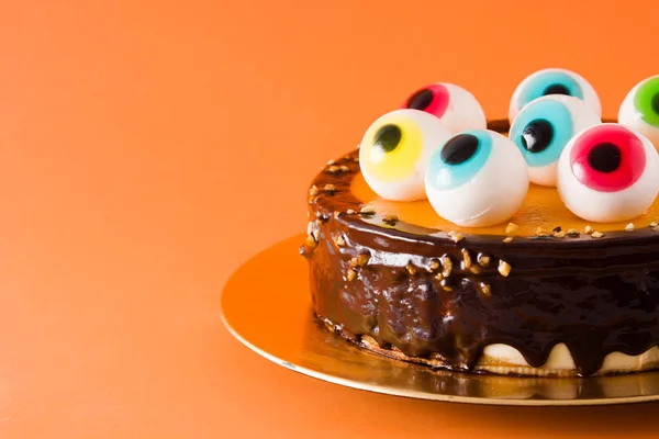 Halloween cake with candy eyes decoration on orange background. Copyspace