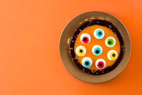 オレンジ色の背景にキャンディの目の装飾とハロウィーンケーキ トップビュー コピースペース — ストック写真