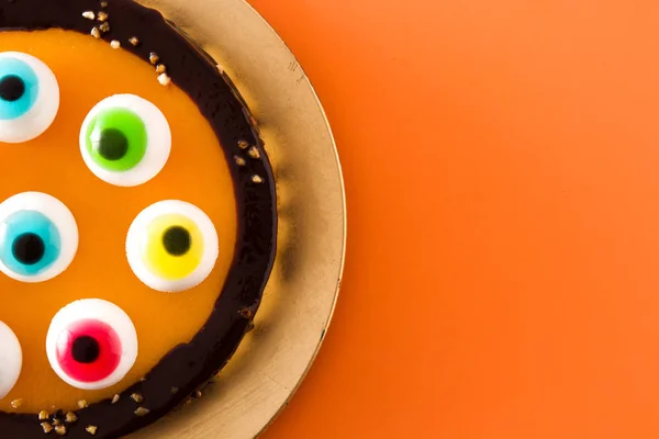 オレンジ色の背景にキャンディの目の装飾とハロウィーンケーキ トップビュー コピースペース — ストック写真