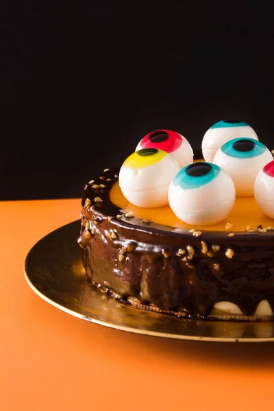Halloween cake with candy eyes decoration on orange and black background. Copyspace