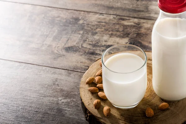 Almond milk in glass and bottle on wooden table. Copyspace