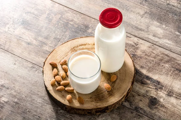 Almond milk in glass and bottle on wooden table.