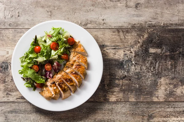 Ahşap masa üzerinde bir tabak üzerinde sebze ile ızgara tavuk göğsü. Üst te. Copyspace