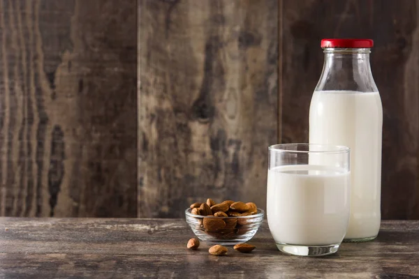 Almond milk in glass and bottle on wooden table. Copy space
