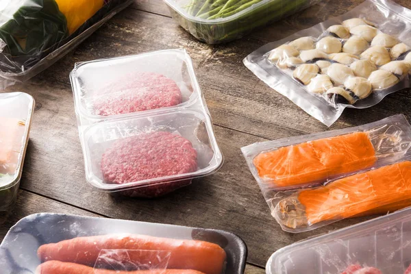 different types of packaged food. Meat, green beans, carrots and salmon on wooden table.