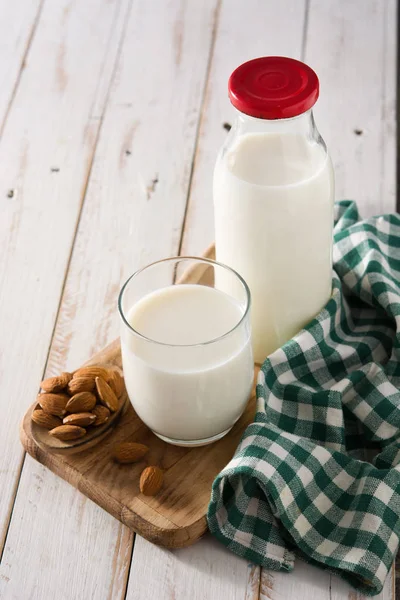 Organic almond milk in glass and bottle on wooden table.