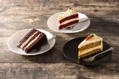 Bir sürü tatlı pasta dilimi. Çikolata, havuç ve ahşap masada kadife kek dilimleri.