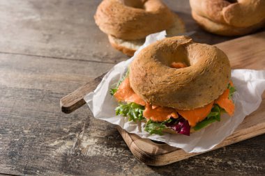 Krem peynirli bagel sandviç, füme somon ve ahşap masada sebze. Boşluğu kopyala