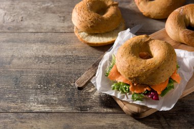 Krem peynirli bagel sandviç, füme somon ve ahşap masada sebze. Boşluğu kopyala