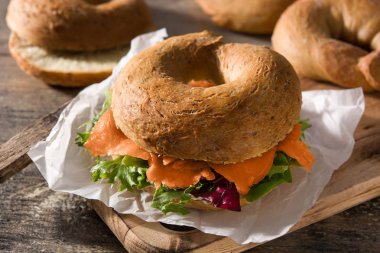 Krem peynirli bagel sandviç, füme somon ve ahşap masada sebze.. 