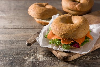 Krem peynirli bagel sandviç, füme somon ve ahşap masada sebze. Boşluğu kopyala