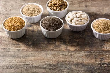 Tahta masadaki kasede farklı tohumlar var. Balkabağı, keten, chia, ayçiçeği ve susam tohumları..