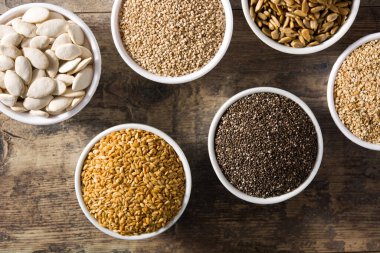 Tahta masadaki kasede farklı tohumlar var. Balkabağı, keten, chia, ayçiçeği ve susam tohumları..