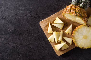 Kesme tahtasında taze ananas dilimleri ve siyah taş arka plan. Boşluğu kopyala