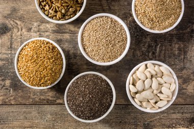 Tahta masadaki kasede farklı tohumlar var. Balkabağı, keten, chia, ayçiçeği ve susam tohumları..