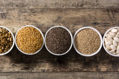 Tahta masadaki kasede farklı tohumlar var. Balkabağı, keten, chia, ayçiçeği ve susam tohumları..