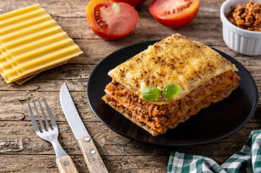 Tahta masadaki siyah tabakta bir parça etli lazanya.