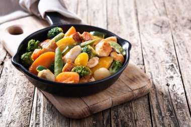 Tavuk kızartmasını sebzelerle karıştırın. Tahta masada demir tavada. Boşluğu kopyala